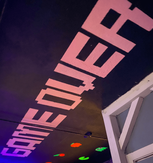 Graffiti on a ceiling reads "GAME OVER" in pink letters, with colorful shapes in the background.