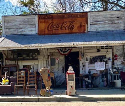 A rustic storefront with vintage Coca-Cola signage, displaying furniture and collectibles outside.
