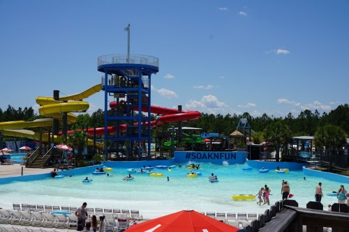 A vibrant water park scene with slides, a wave pool, and visitors enjoying the sun and water activities.