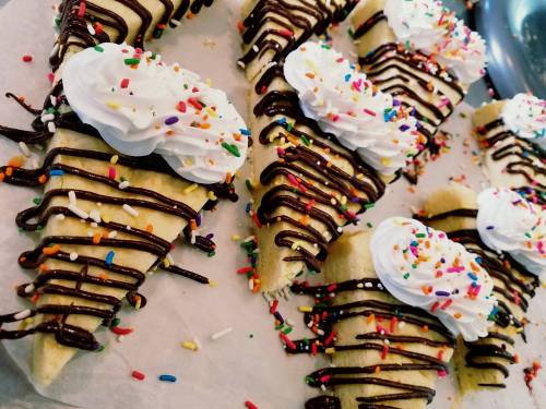 Delicious dessert cones topped with whipped cream, chocolate drizzle, and colorful sprinkles on a white surface.