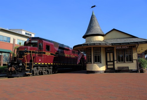 A vintage red train at a charming station with a pointed roof, set in a quaint town.