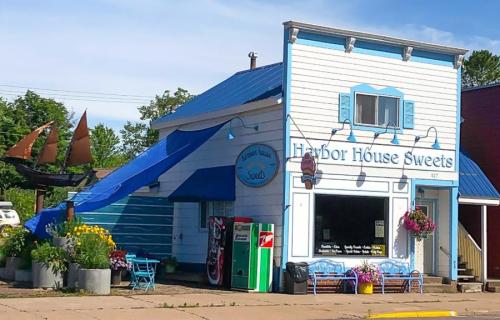 A charming blue and white building with a slide, featuring "Harbor House Sweets" signage and colorful flowers outside.