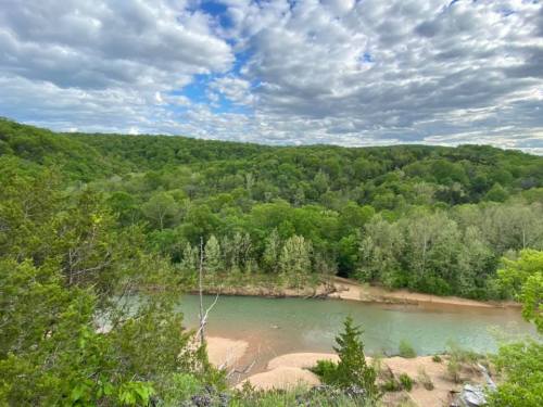 A scenic view of a river winding through lush green trees under a partly cloudy sky.