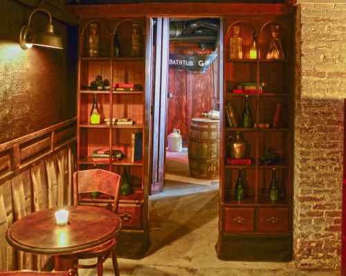 A cozy, dimly lit room with wooden shelves, a small table, and a doorway leading to a rustic space with a barrel.