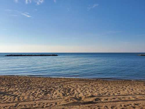 A serene beach scene with calm blue water, a sandy shore, and a clear sky.