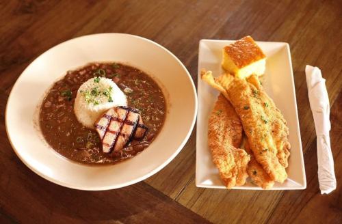 A plate of rice with grilled meat and beans, alongside fried fish and cornbread on a separate dish.