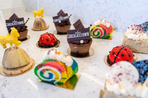 A variety of colorful desserts, including chocolate cups, rainbow cake, and ladybug treats, displayed on a marble surface.