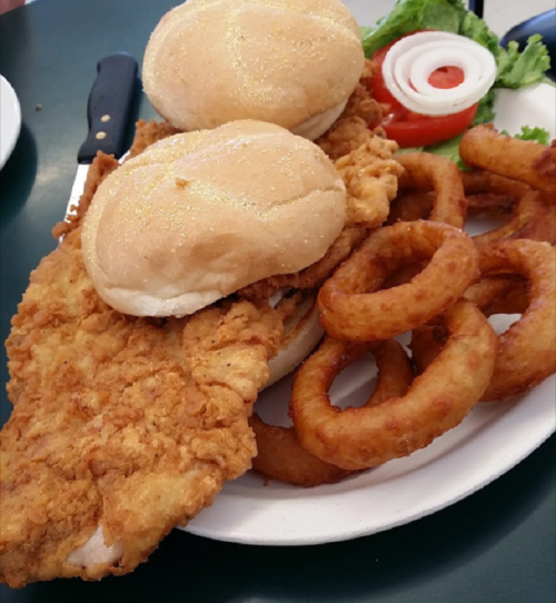 A plate with two fried chicken sandwiches, onion rings, lettuce, tomato, and onion slices.