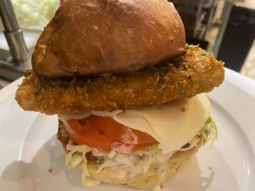 A close-up of a sandwich featuring a crispy chicken fillet, lettuce, tomato, cheese, and a toasted bun on a plate.