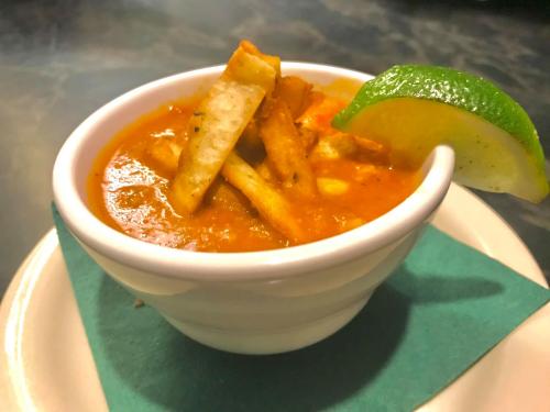 A bowl of soup topped with crispy tortilla strips and a lime wedge, served on a plate with a green napkin.