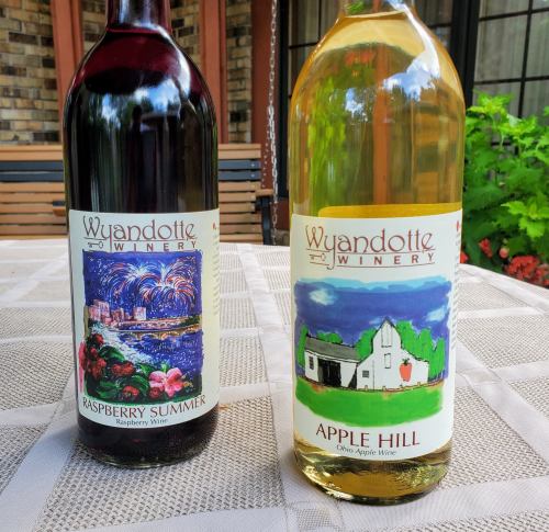 Two wine bottles on a table: one red labeled "Raspberry Summer" and one white labeled "Apple Hill."