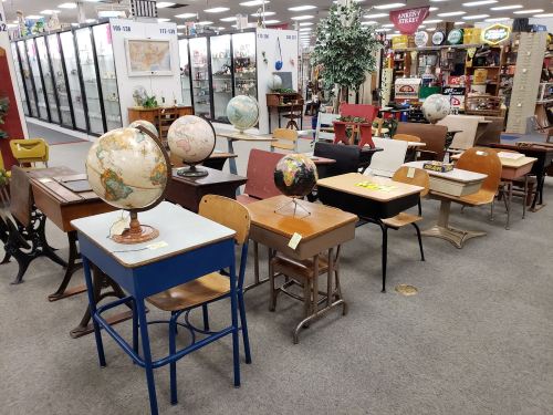 A row of vintage school desks and globes displayed in an antique shop.