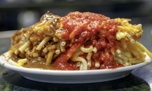 A plate of macaroni topped with chili and a rich red sauce, showcasing a hearty and colorful meal.