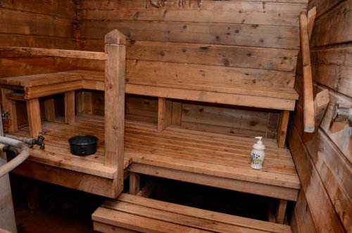A wooden sauna interior with benches, a small pot, and a bottle of soap on a shelf. Warm, rustic atmosphere.