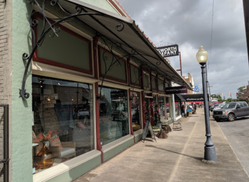 A street view of a storefront with decorative awnings and a sidewalk, featuring plants and outdoor seating.