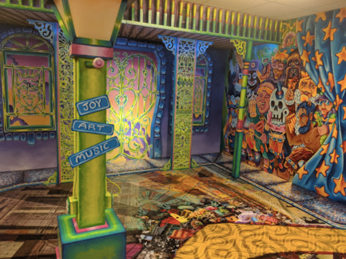Colorful room with vibrant murals, pillars labeled "Joy," "Art," and "Music," and a lively, artistic atmosphere.