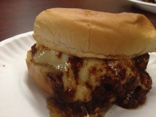 A close-up of a sandwich with a soft bun filled with a savory meat mixture and melted cheese, served on a paper plate.