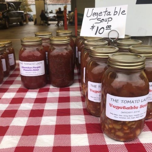 Jars of vegetable soup for sale on a checkered tablecloth, with a sign listing the price at $10.