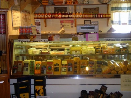 A deli display featuring various cheeses and products, with jars and signs on the wall above.
