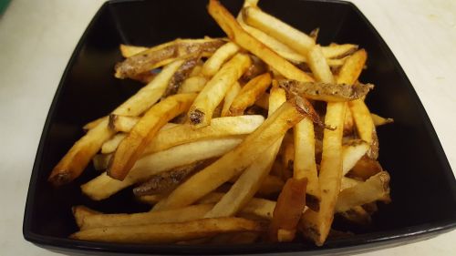 A black bowl filled with golden-brown French fries, varying in thickness and crispiness.