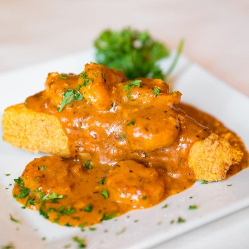 A plate of golden fried fish topped with a rich, spicy sauce and garnished with fresh herbs.