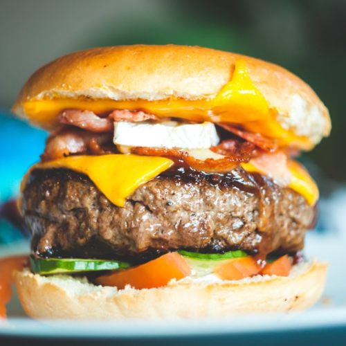 A close-up of a juicy burger with cheese, bacon, lettuce, and tomato, served in a soft bun.