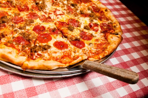 A close-up of a pepperoni and sausage pizza on a metal tray, resting on a red and white checkered tablecloth.