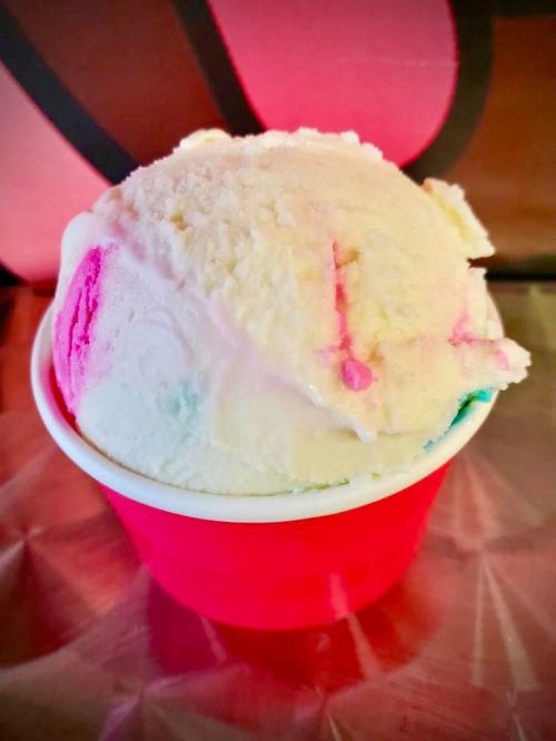 A colorful scoop of ice cream in a red cup, featuring swirls of pink and blue against a creamy white base.