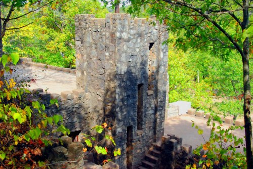 A stone tower surrounded by lush green trees and autumn foliage, set in a natural landscape.