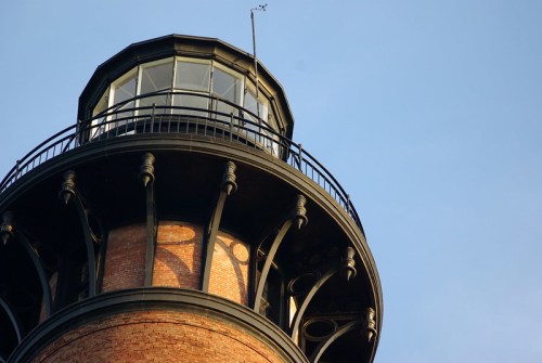 Close-up of a lighthouse tower with a glass lantern room against a clear blue sky.