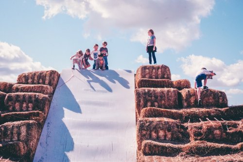 Children playing on a large haystack slide under a blue sky with fluffy clouds.
