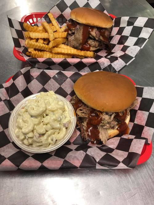 Two pulled pork sandwiches with barbecue sauce, crinkle-cut fries, and a bowl of macaroni salad in a red basket.