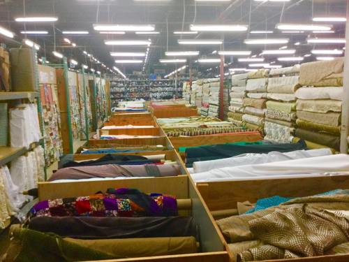 A spacious fabric store with rows of colorful textiles neatly arranged on shelves and tables under bright lights.