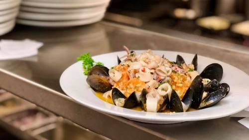 A plate of seafood risotto topped with mussels and squid, garnished with parsley, on a kitchen counter.