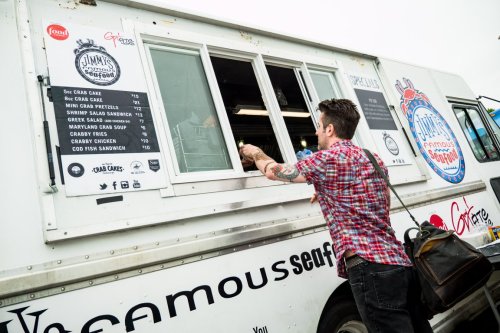 A person orders food at a seafood food truck with a menu displayed on the side.