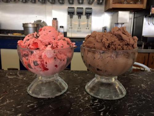 Two ice cream scoops in glass bowls: one pink with chocolate bits, the other rich brown chocolate.