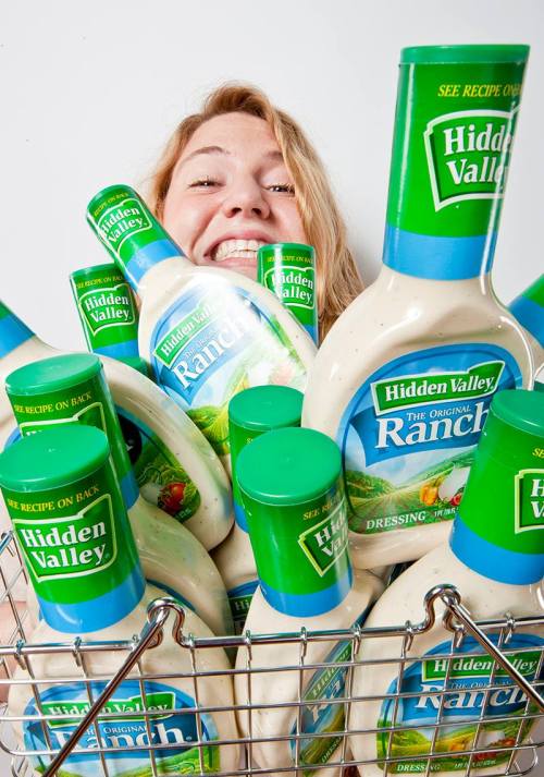 A smiling person surrounded by bottles of Hidden Valley Ranch dressing in a shopping cart.