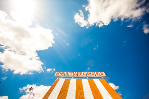 A bright blue sky with fluffy clouds above a Whataburger restaurant sign, featuring orange and white stripes.