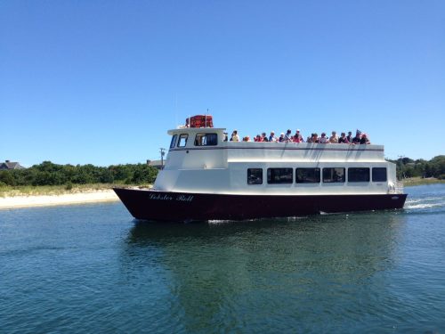 A passenger boat named "Fisher Bell" sails on calm waters, with people enjoying the ride under a clear blue sky.