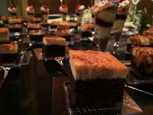 A variety of desserts, including layered cakes and parfaits, arranged on a table with decorative garnishes.