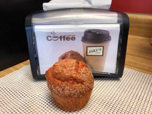 A freshly baked muffin sits in front of a coffee cup display at a café.
