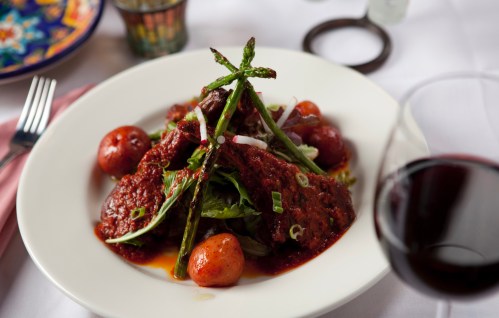 A plate of meat with asparagus, potatoes, and greens, accompanied by a glass of red wine.
