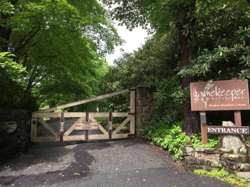 A wooden gate at the entrance of a restaurant, surrounded by lush greenery and a sign that reads "Gamekeeper."
