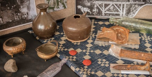 A display of various historical artifacts, including pottery, metal objects, and a patterned cloth background.