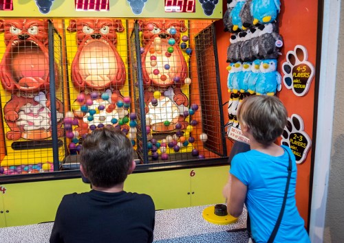 Two children play a colorful arcade game featuring large cartoonish animals and colorful balls.