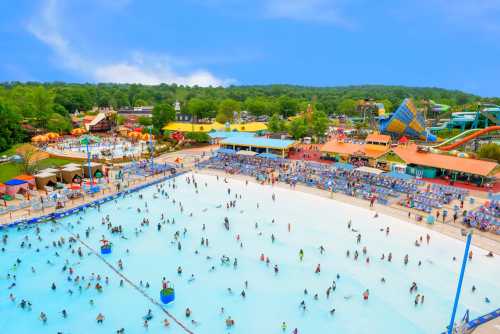 Aerial view of a busy water park with a large wave pool and colorful attractions under a blue sky.