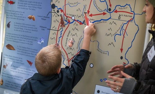 A child points at a map while an adult observes, highlighting locations in a nature-themed educational display.