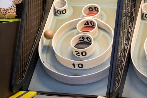 A close-up of a skee-ball game with balls rolling towards numbered scoring holes.