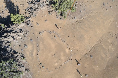 Aerial view of a rocky landscape with a circular arrangement of stones and two people in the distance.