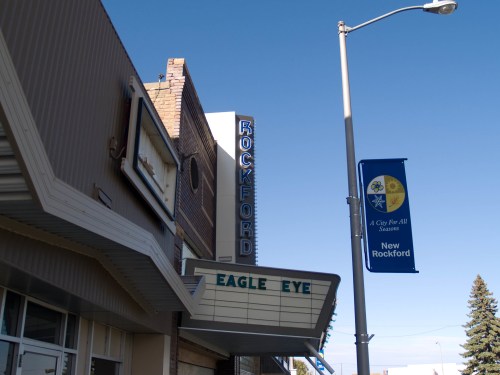 A vintage theater marquee displays "EAGLE EYE" with a "ROCKFORD" sign above, under a clear blue sky.